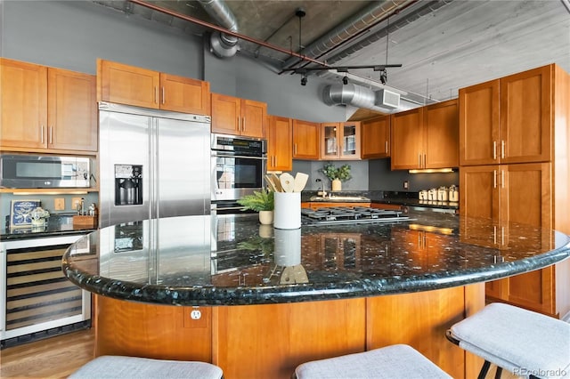 kitchen with a breakfast bar area, dark stone countertops, stainless steel appliances, a high ceiling, and beverage cooler