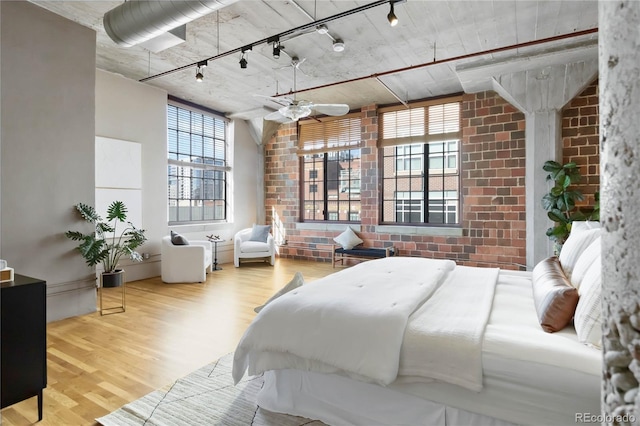 bedroom with hardwood / wood-style floors, rail lighting, and brick wall