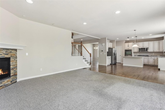 3823 Horiuchi St, Brighton, CO 80601 - unfurnished living room featuring dark colored carpet, recessed lighting, stairway, baseboards, and a fireplace