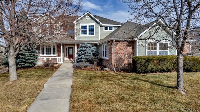 traditional home featuring brick siding, a porch, a shingled roof, and a front yard