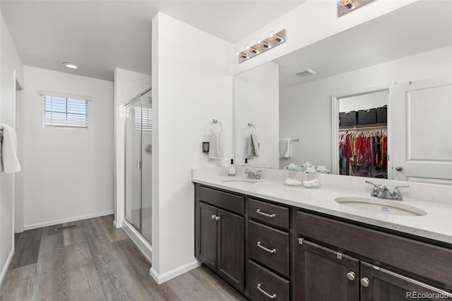 full bath with double vanity, wood finished floors, a stall shower, and a sink