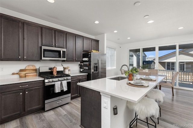 kitchen featuring light wood-style flooring, a sink, dark brown cabinets, appliances with stainless steel finishes, and a kitchen bar