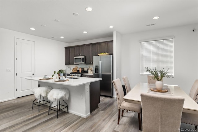 kitchen with stainless steel appliances, a breakfast bar, a kitchen island with sink, and light wood finished floors