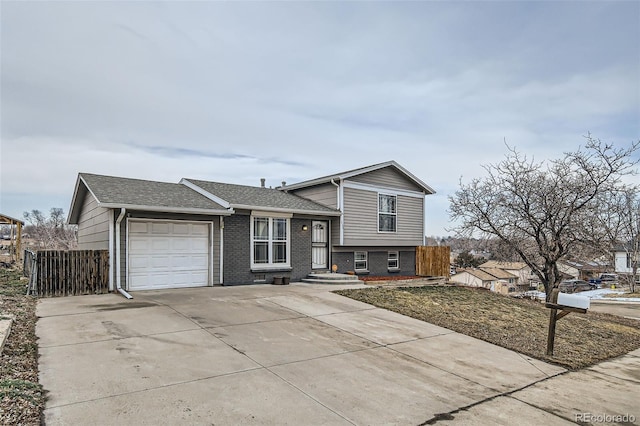 split level home featuring a garage, brick siding, a shingled roof, fence, and driveway