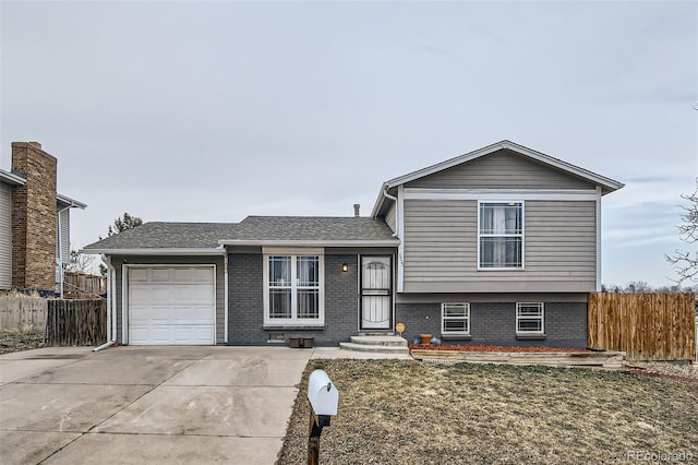 split level home featuring a garage, fence, concrete driveway, and brick siding