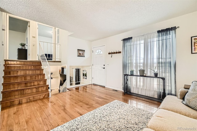 living room with visible vents, a textured ceiling, stairway, and wood finished floors