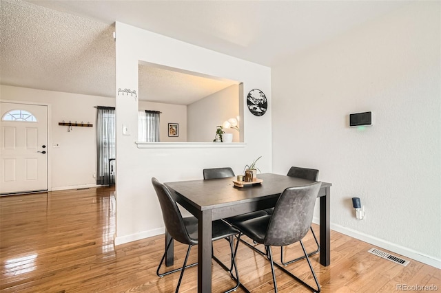 dining room with light wood finished floors, a wealth of natural light, visible vents, a textured ceiling, and baseboards