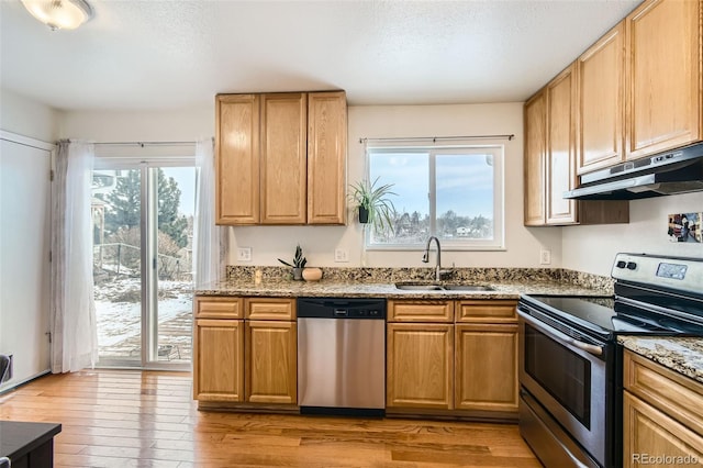 kitchen featuring light stone counters, under cabinet range hood, a sink, appliances with stainless steel finishes, and light wood finished floors