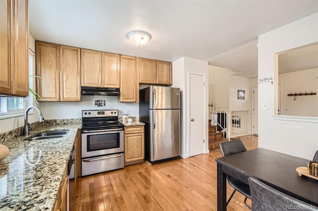 kitchen featuring light stone counters, appliances with stainless steel finishes, light wood-style floors, a sink, and under cabinet range hood