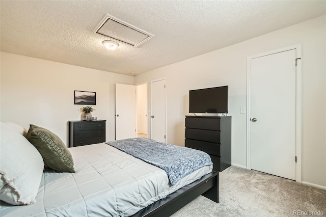 bedroom featuring a textured ceiling, attic access, and light colored carpet