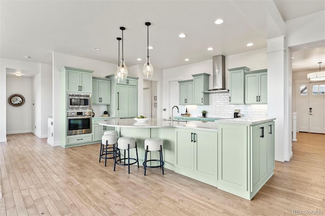 9510 Orion Way, Arvada, CO 80007 - kitchen featuring stainless steel appliances, wall chimney range hood, green cabinets, light countertops, and decorative backsplash