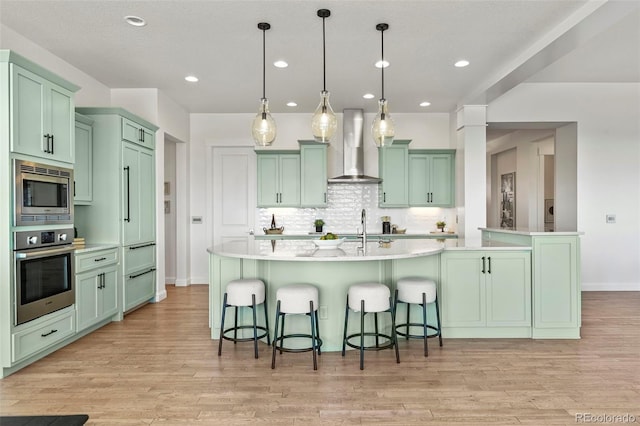 9510 Orion Way, Arvada, CO 80007 - kitchen featuring stainless steel appliances, wall chimney exhaust hood, green cabinets, light wood-style floors, and recessed lighting