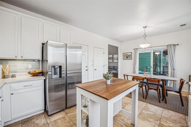 kitchen featuring stainless steel fridge with ice dispenser, tasteful backsplash, decorative light fixtures, light tile patterned flooring, and white cabinets