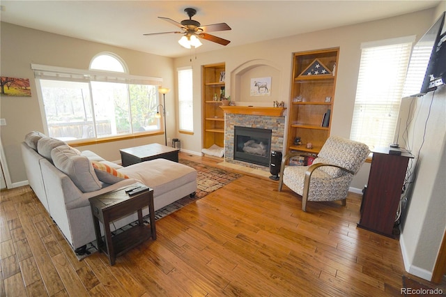 living room with baseboards, a stone fireplace, hardwood / wood-style floors, and ceiling fan