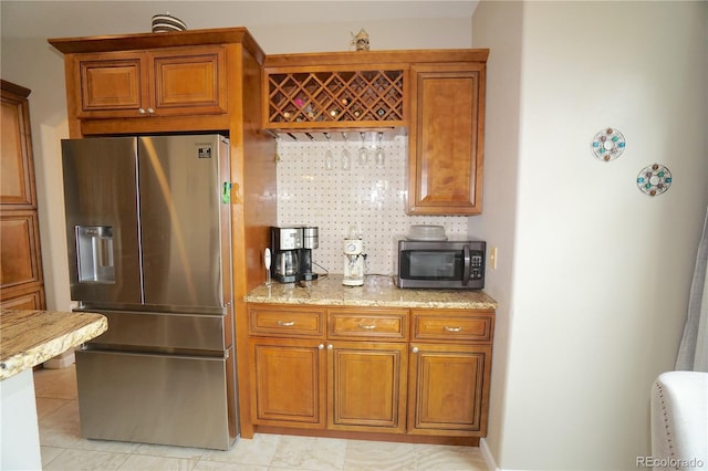 kitchen with light stone countertops, stainless steel appliances, light tile patterned floors, and brown cabinets