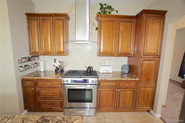 kitchen with stainless steel gas range, wall chimney range hood, stone countertops, and brown cabinets