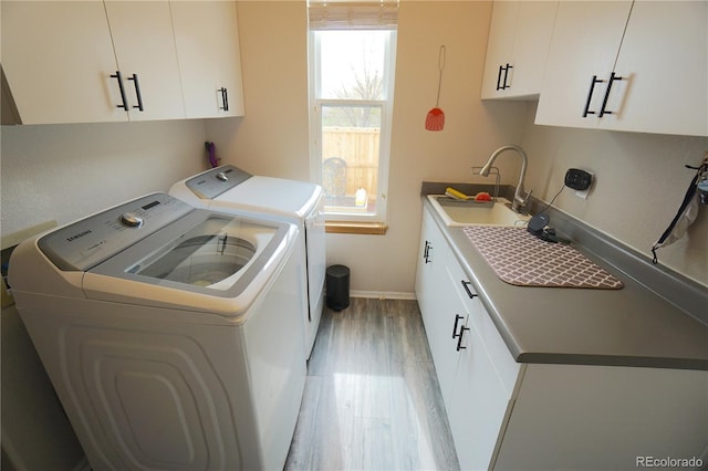 laundry area with baseboards, a sink, washing machine and clothes dryer, light wood-style floors, and cabinet space