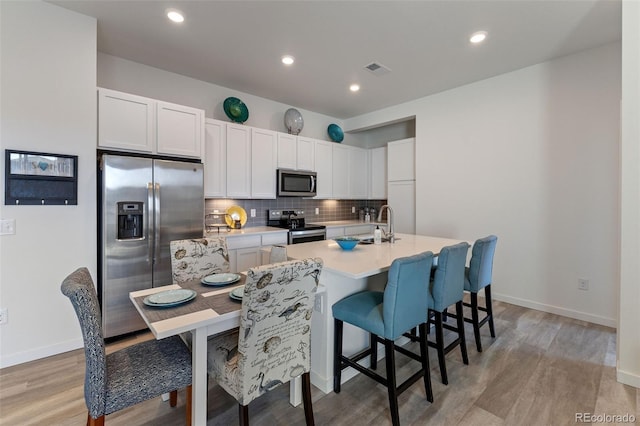 kitchen featuring white cabinetry, light hardwood / wood-style flooring, appliances with stainless steel finishes, a kitchen island with sink, and decorative backsplash