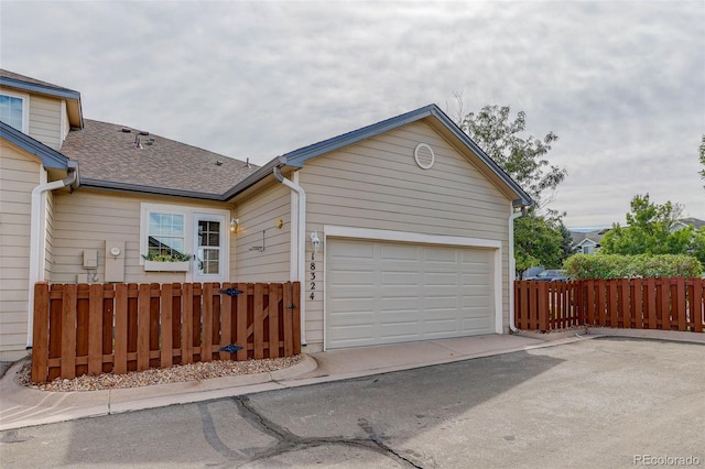 view of front facade with an attached garage, a shingled roof, fence, and aphalt driveway