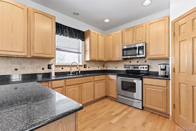 kitchen featuring stainless steel appliances, light wood-style floors, light brown cabinets, a sink, and dark stone countertops