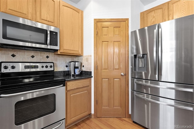 kitchen with light wood finished floors, decorative backsplash, appliances with stainless steel finishes, dark stone countertops, and light brown cabinetry