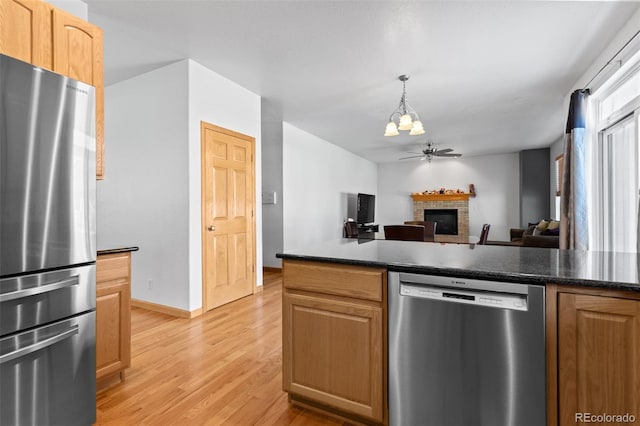 kitchen with a fireplace, dark countertops, appliances with stainless steel finishes, open floor plan, and ceiling fan