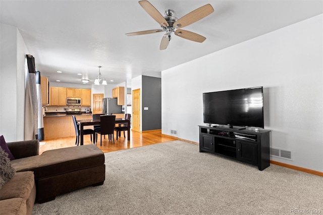 living area featuring light carpet, baseboards, visible vents, and a ceiling fan