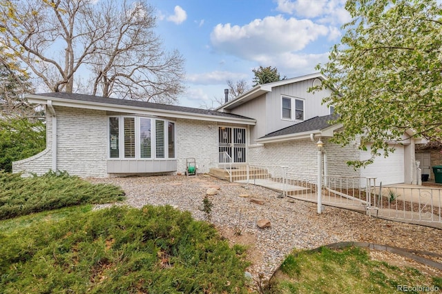 back of property with driveway, an attached garage, brick siding, and board and batten siding