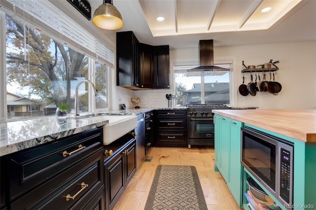 kitchen with wood counters, light hardwood / wood-style flooring, ventilation hood, a tray ceiling, and appliances with stainless steel finishes