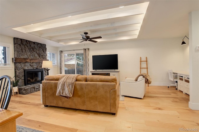 living room featuring beamed ceiling, ceiling fan, a fireplace, and light hardwood / wood-style flooring