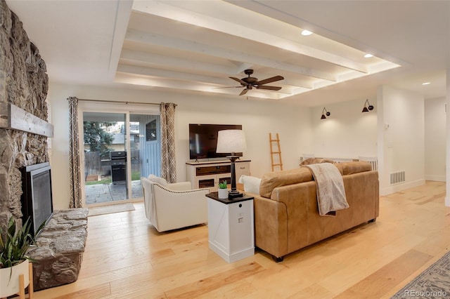 living room with a raised ceiling, a fireplace, ceiling fan, and light hardwood / wood-style flooring