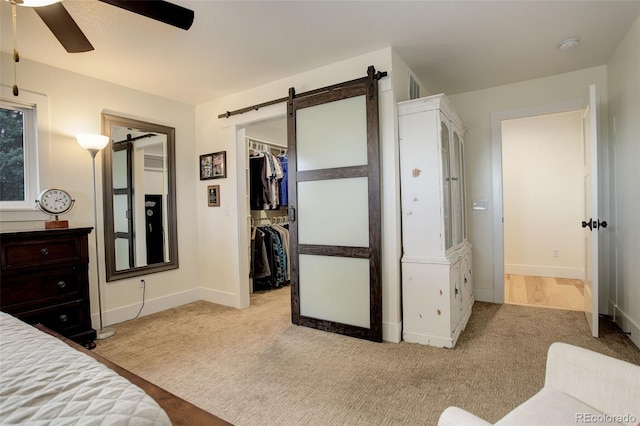 carpeted bedroom with a barn door, a closet, a spacious closet, and ceiling fan