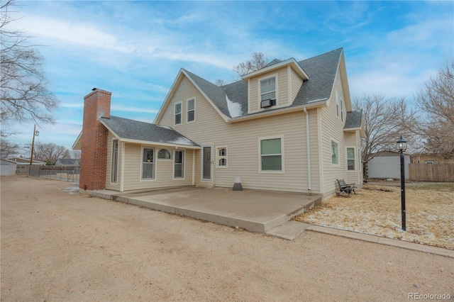 back of house with a patio area, fence, roof with shingles, and a chimney