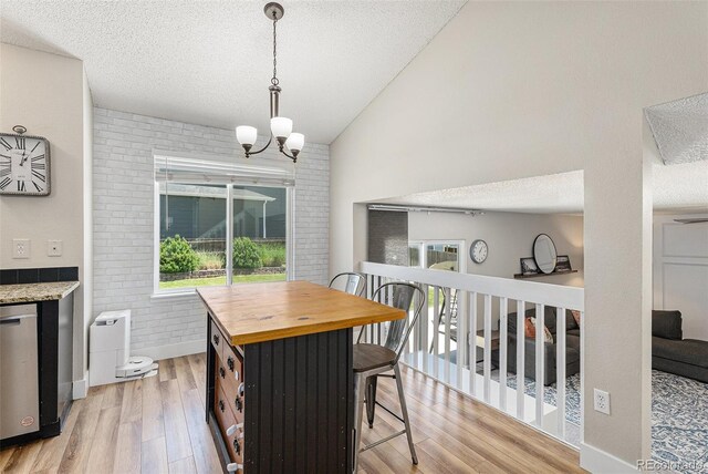 5102 S Lisbon Way, Centennial, CO 80015 - dining room featuring light wood-type flooring, a textured ceiling, a chandelier, vaulted ceiling, and brick wall