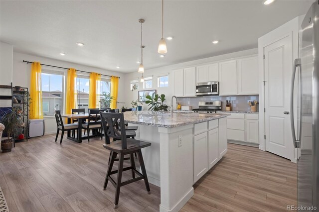 8372 Bijou Creek Ave, Littleton, CO 80125 - kitchen featuring appliances with stainless steel finishes, light wood-type flooring, recessed lighting, tasteful backsplash, and white cabinetry