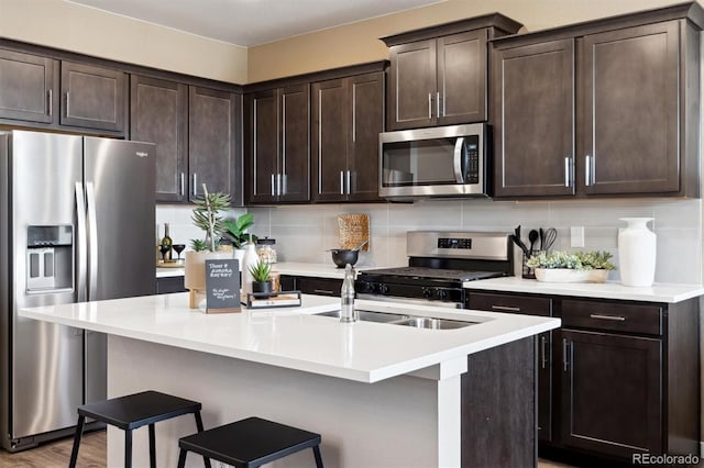 kitchen with stainless steel appliances, decorative backsplash, a breakfast bar, dark brown cabinetry, and a center island with sink