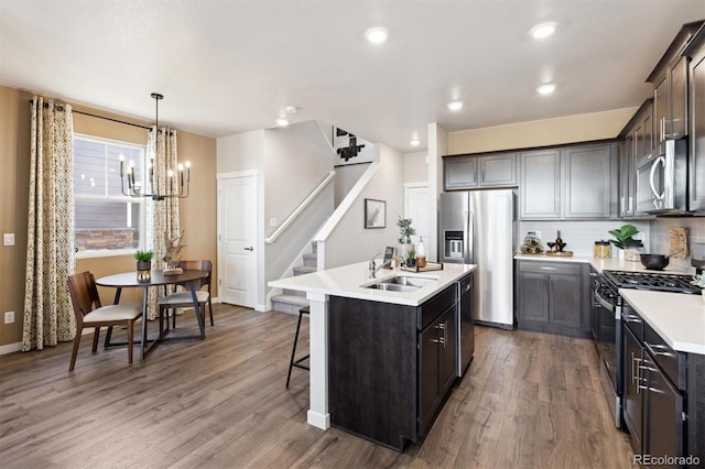 kitchen with appliances with stainless steel finishes, a sink, an island with sink, a chandelier, and wood finished floors