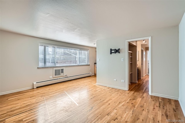 empty room featuring light wood finished floors, baseboard heating, baseboards, and visible vents