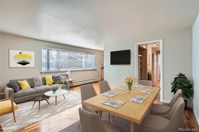 dining area with wood finished floors, baseboards, baseboard heating, and a textured ceiling