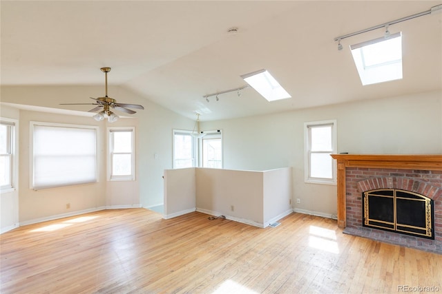 unfurnished living room with light wood finished floors, baseboards, lofted ceiling with skylight, a fireplace, and rail lighting