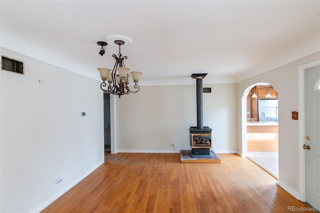 unfurnished living room featuring baseboards, visible vents, a wood stove, a notable chandelier, and light wood-type flooring