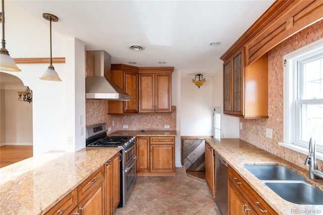 kitchen with a sink, wall chimney exhaust hood, brown cabinetry, and stainless steel appliances