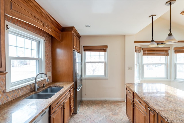 kitchen featuring baseboards, stainless steel refrigerator, hanging light fixtures, a sink, and brown cabinets