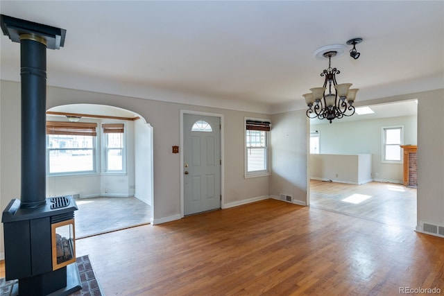 foyer entrance with a wood stove, wood finished floors, visible vents, and arched walkways