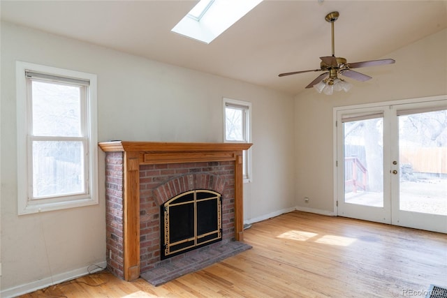 unfurnished living room featuring a ceiling fan, wood finished floors, a skylight, baseboards, and a brick fireplace