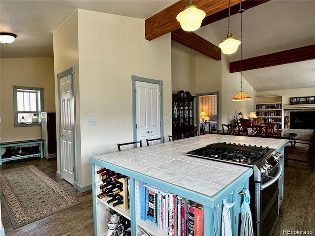 kitchen with hanging light fixtures, stainless steel gas range, beamed ceiling, dark hardwood / wood-style floors, and tile countertops