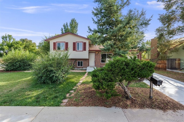 tri-level home with a front yard, brick siding, and fence