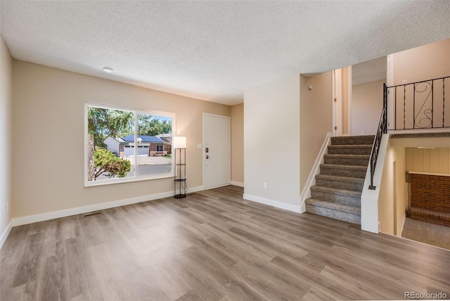 interior space with a textured ceiling, stairs, baseboards, and wood finished floors