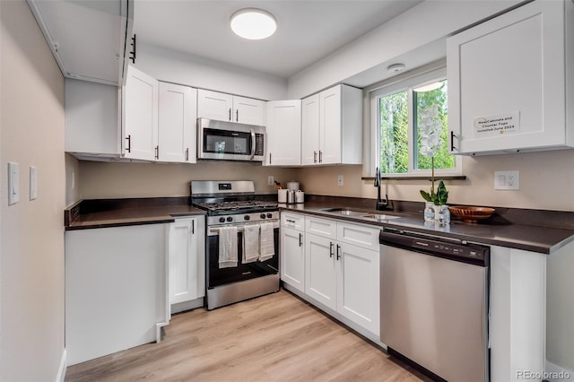 kitchen featuring light wood-style flooring, a sink, white cabinetry, appliances with stainless steel finishes, and dark countertops