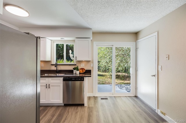 kitchen with dark countertops, visible vents, appliances with stainless steel finishes, white cabinets, and a sink